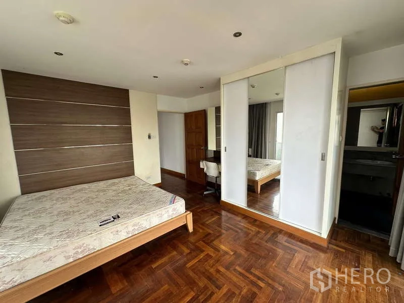 公寓 出租在Watthana, Bangkok - 卧室设特色墙、镜面衣柜与木地板，连通套卫入口。