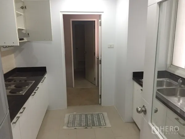 公寓 出租在Khlong Toei, Bangkok - 走廊式厨房，黑色石材台面、电炉和白色橱柜。