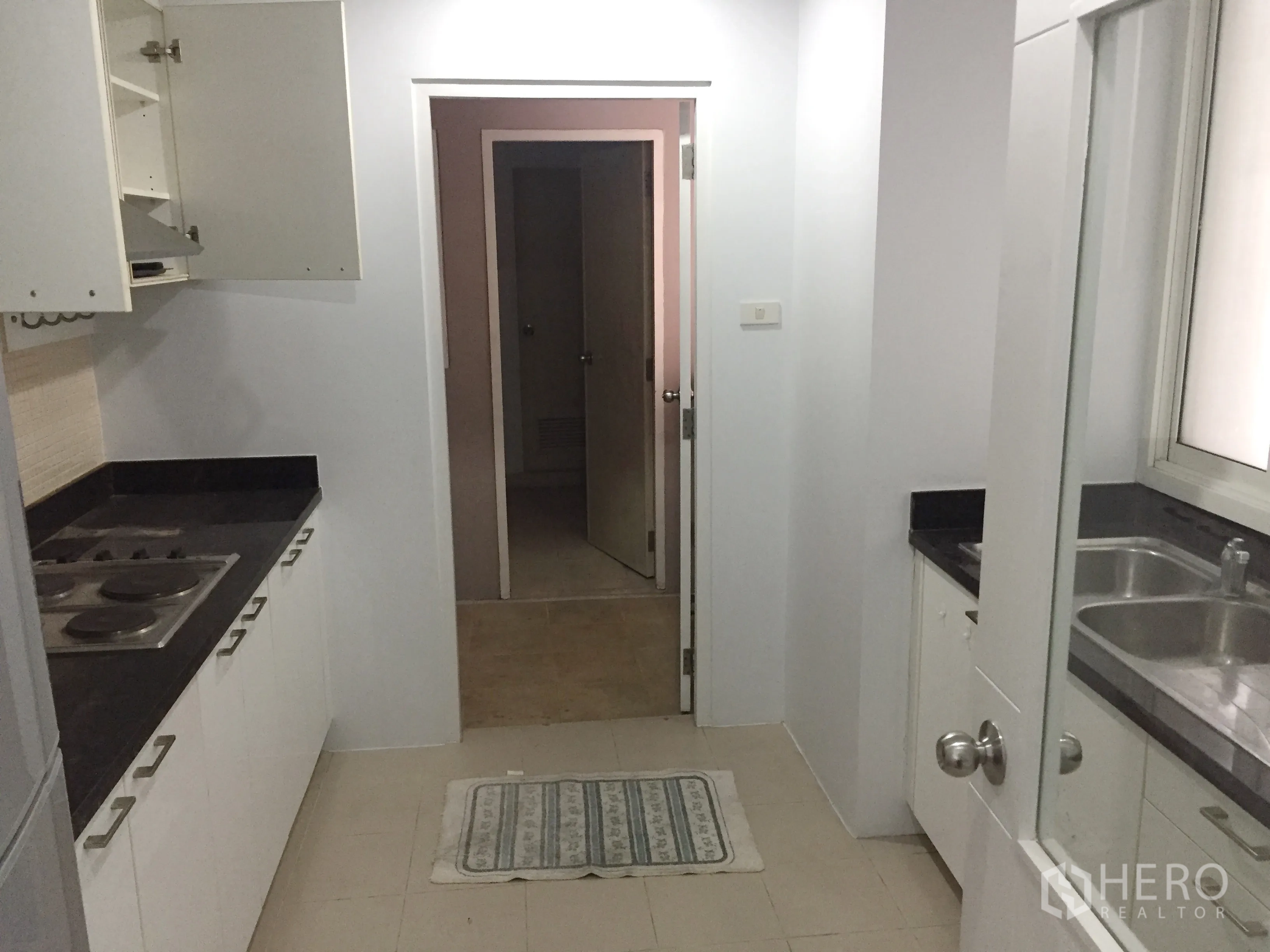公寓 出租在Khlong Toei, Bangkok - 走廊式厨房，黑色石材台面、电炉和白色橱柜。