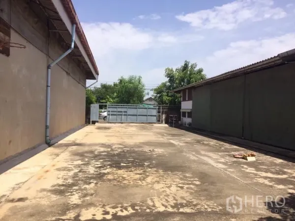 Warehouse for rent in Samut Prakan - Wide paved yard between warehouse buildings with a secure gate ahead.