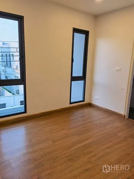 Detached House for rent in Bang Phli, Samut Prakan - Empty bedroom with wood flooring and tall black-framed windows.