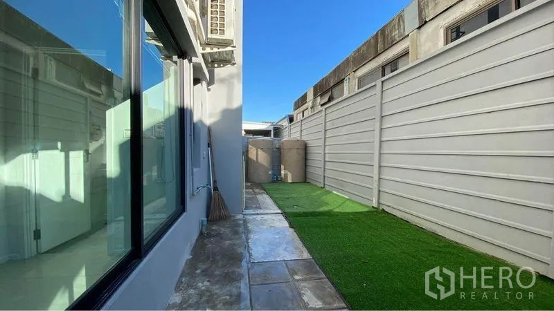 Retail Space for sale in Bang Na, Bangkok - Narrow side service yard with artificial grass and a concrete walkway behind a high fence.