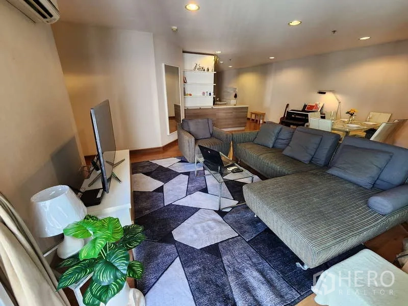 คอนโด ให้เช่าในHuai Khwang, Bangkok - ห้องนั่งเล่นแบบเปิดโล่ง โซฟาเข้ามุม ทีวี และพรมลายเรขาคณิตบนพื้นไม้