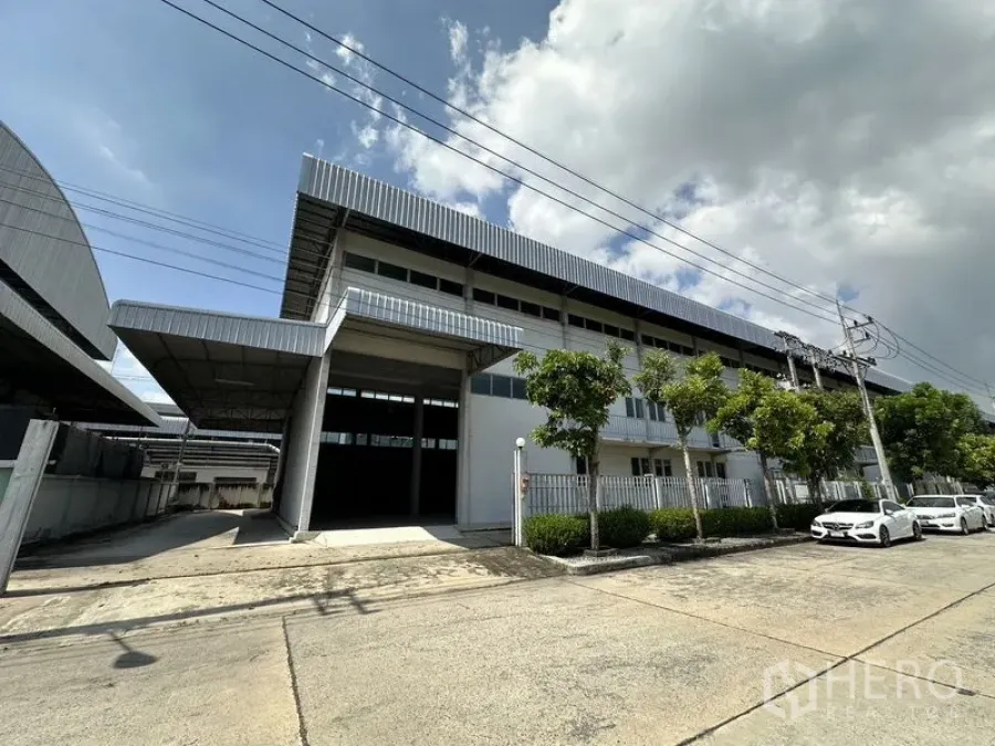 Factory for rent in Lam Luk Ka, Pathum Thani - Modern factory exterior with wide covered loading bay and gated frontage on a quiet street.