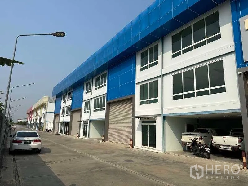 Warehouse for rent in Bang Phli, Samut Prakan - Row of warehouse units along an internal road with parking and blue facade panels.