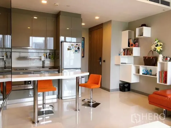 Condominium for rent in Bang Rak, Bangkok - Modern kitchen with island, two orange bar stools and floating shelves.