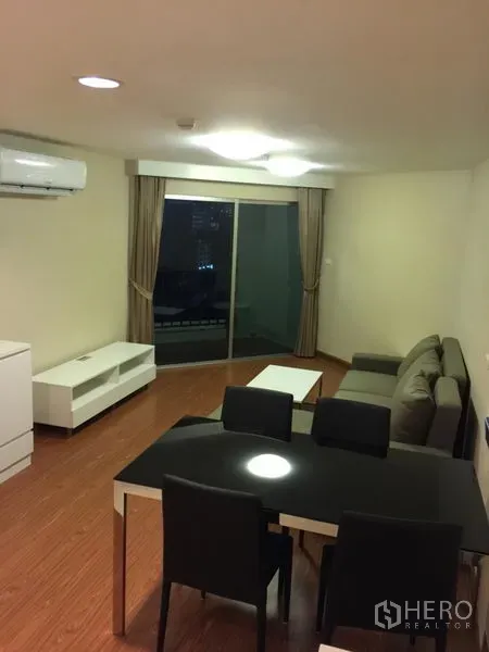 คอนโด ให้เช่าในHuai Khwang, Bangkok - ห้องนั่งเล่นพร้อมโซฟาสีเทา ชุดทานอาหาร และประตูกระจกบานเลื่อนออกระเบียงยามค่ำ