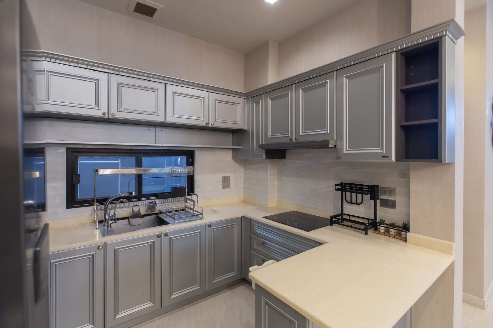 Detached House for rent in Lat Phrao, Bangkok - L-shaped kitchen with shaker cabinets, solid countertops, induction hob, and window.