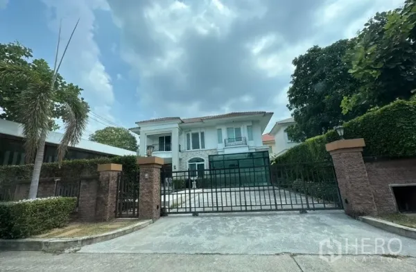 独立式住宅 出售 - 带砖砌围墙与滑动铁门的房屋正面，整齐绿篱与成树，阴天景色。