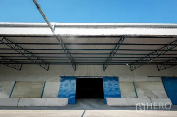 Warehouse for rent in Pathum Thani - Warehouse exterior with covered loading dock and blue sliding doors under a steel canopy.