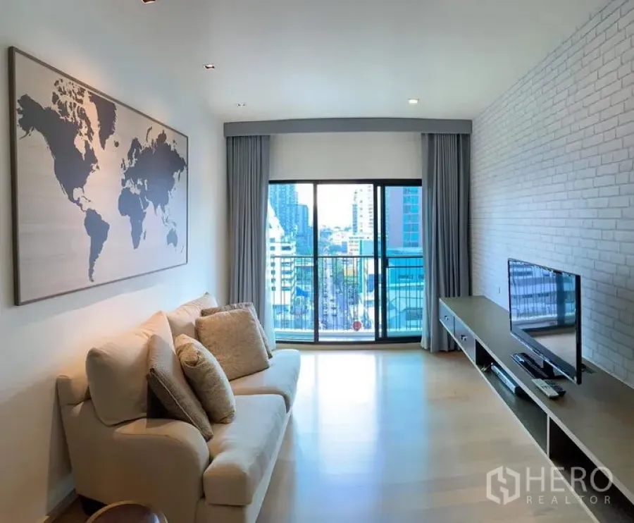 Condominium for rent in Phaya Thai, Bangkok - Wide living space with light wood floors, brick accent wall, TV unit and full-height windows.