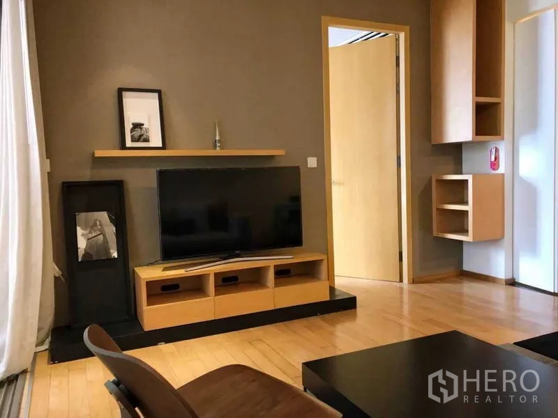 Condominium for rent in Watthana, Bangkok - TV wall with floating shelf and built-in cabinet on warm wood flooring.