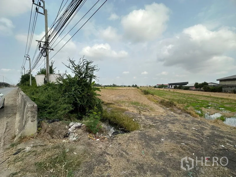 ที่ดิน ขายในBang Bua Thong, Nonthaburi - มุมแปลงที่ดินพื้นดินแห้ง มีคูน้ำและต้นไม้ ริมถนนใหญ่และสาธารณูปโภค