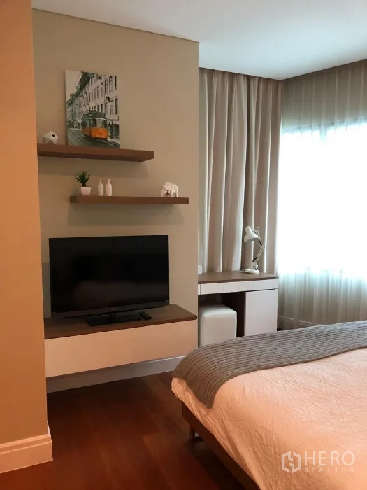 Condominium for rent or sale in Khlong Toei, Bangkok - Bedroom corner featuring wall-mounted TV, floating shelves and compact work desk.