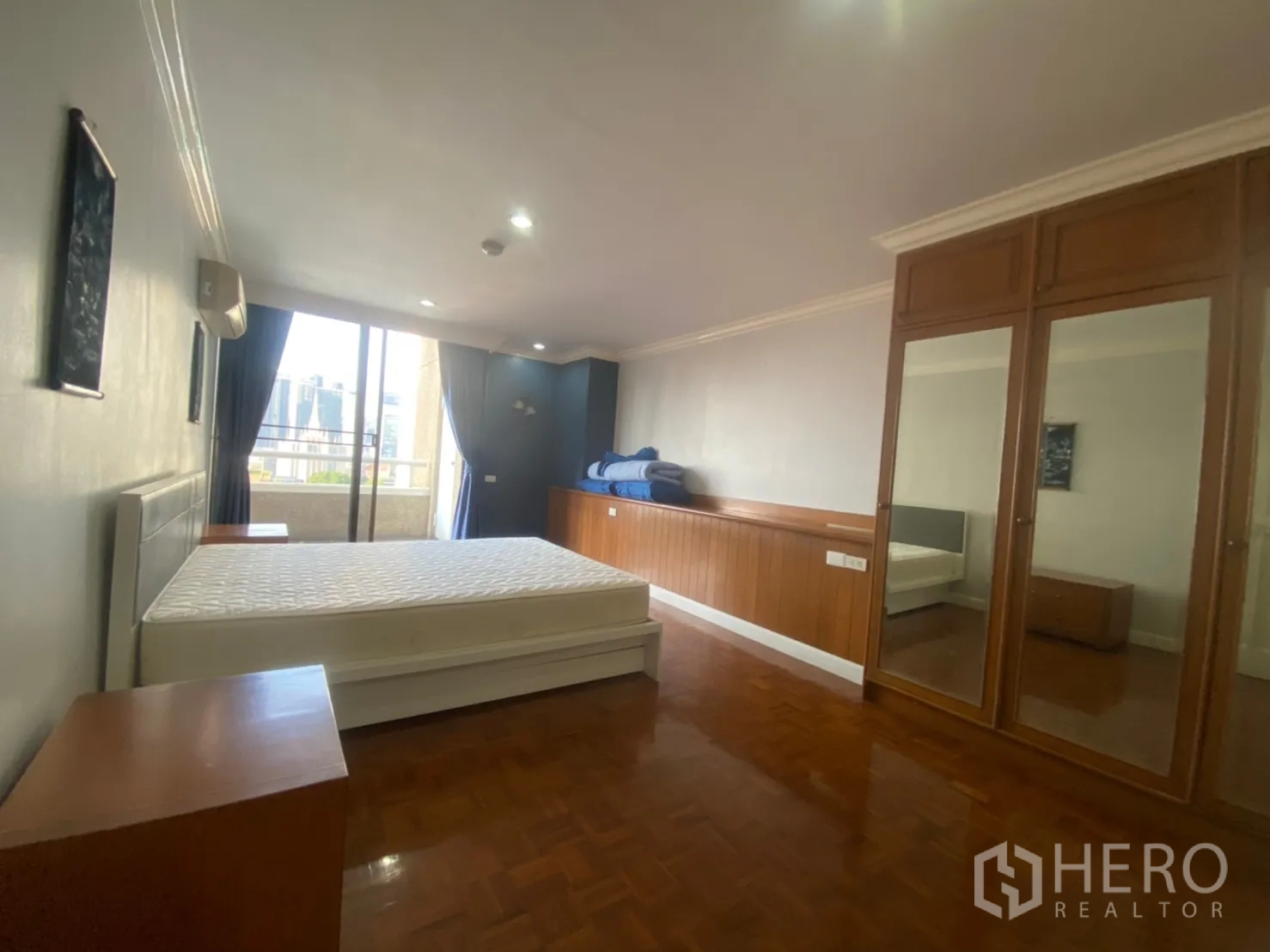 Condominium for rent or sale in Watthana, Bangkok - Spacious bedroom with mirrored wardrobes, wood paneling and sliding doors to a city-view balcony.