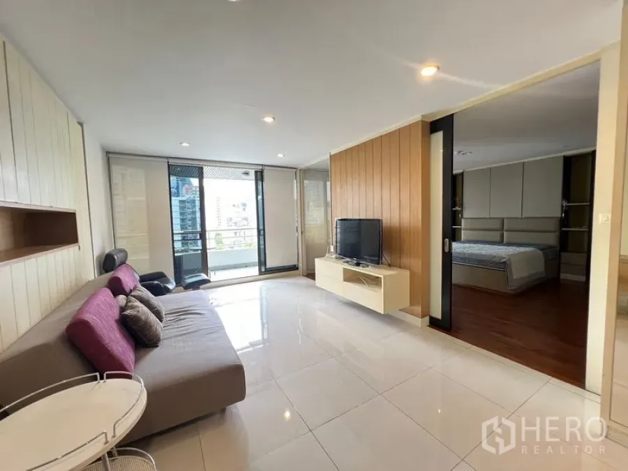 Condominium for rent or sale in Khlong Toei, Bangkok - Living area with sofa and TV beside sliding doors to the bedroom and balcony.