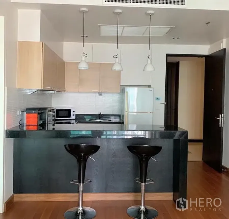 Condominium for rent in Pathum Wan, Bangkok - Open kitchen with black breakfast bar, pendant lights, and built-in cabinets in a Pathum Wan condo near BTS Chitlom.