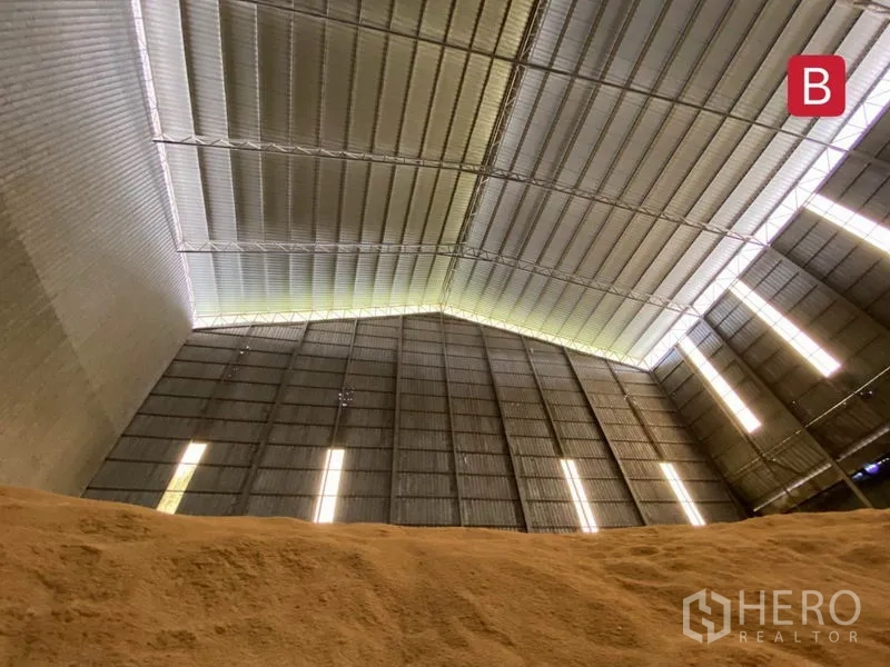Factory for rent in Chachoengsao - Close view of the high metal roof and vertical light panels above a bulk material pile.