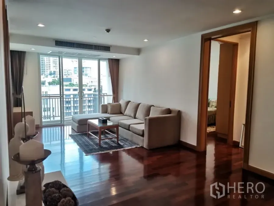 Condominium for rent in Khlong Toei, Bangkok - Living room with an L-shaped sofa, coffee table, and sliding doors opening to a balcony with urban views.