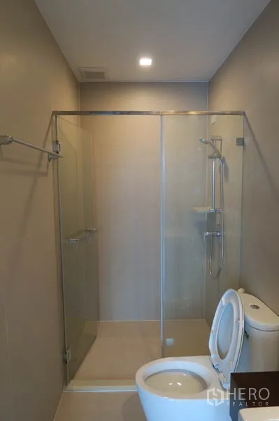 Townhouse for rent in Suan Luang, Bangkok - Bathroom featuring a clear glass shower enclosure and toilet in warm neutral tones.