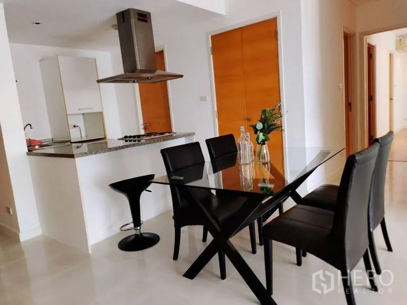Condominium for rent in Watthana, Bangkok - Dining area with glass table for four beside a breakfast bar and range-hood island kitchen.