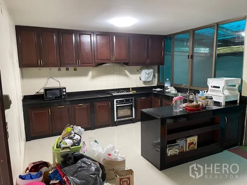Home Office for rent in Watthana, Bangkok - Full kitchen showing gas hob, oven, black counters and overhead cabinets.