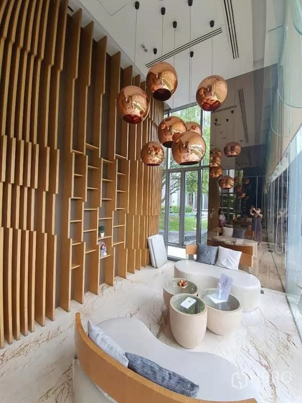 公寓 出租在Watthana, Bangkok - 挑高大堂，雕塑感木质墙面与铜色吊灯。
