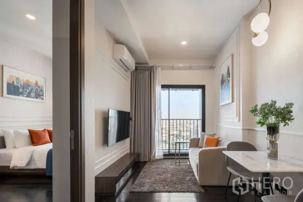 Condominium for rent in Watthana, Bangkok - Bright living room with sofa, TV wall and balcony, plus adjoining bedroom.