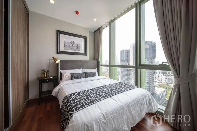 公寓 出租在Ratchathewi, Bangkok - 转角卧室配落地玻璃，灰色床头板，俯瞰城市天际线。