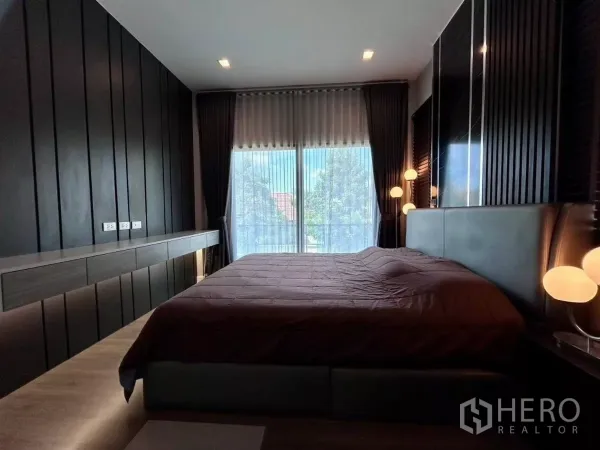 独立式住宅 出租在Bang Phli, Samut Prakan - 主卧采用深色木质墙面，大床与通高窗户连接阳台。