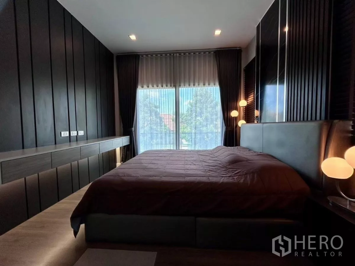 独立式住宅 出租在Bang Phli, Samut Prakan - 主卧采用深色木质墙面，大床与通高窗户连接阳台。