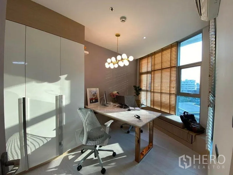 Condominium for sale in Huai Khwang, Bangkok - Bright home office with large desk, modern chandelier, floor-to-ceiling windows with wooden blinds and city outlook.