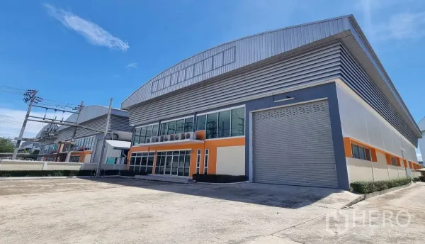 工厂 出租在Samut Prakan - 现代工厂外观，带玻璃幕墙办公室与大型卷帘门（Phraeksa）。