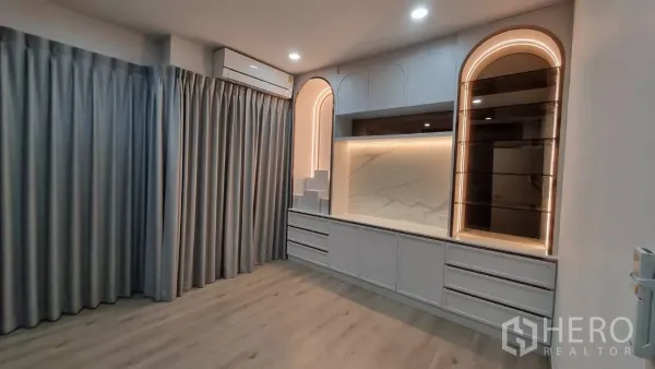 Home Office for rent in Lat Phrao, Bangkok - Custom built-in cabinetry with arched shelves and soft LED lighting beside full-length curtains.