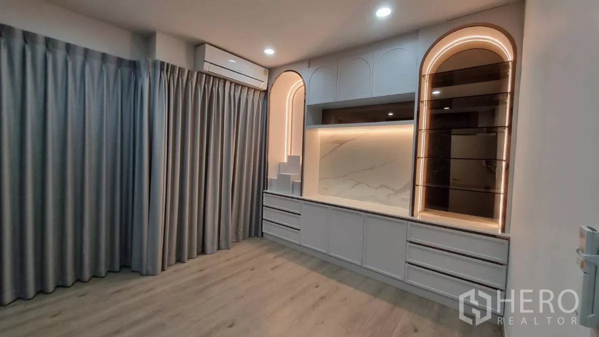 Home Office for rent in Lat Phrao, Bangkok - Custom built-in cabinetry with arched shelves and soft LED lighting beside full-length curtains.