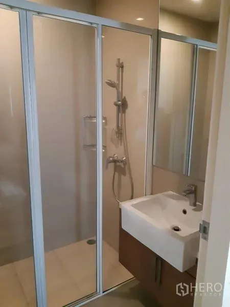 Condominium for rent in Phaya Thai, Bangkok - Modern bathroom featuring a glass-enclosed shower, white basin, and mirrored cabinet.