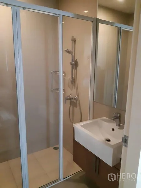 Condominium for rent in Phaya Thai, Bangkok - Modern bathroom featuring a glass-enclosed shower, white basin, and mirrored cabinet.