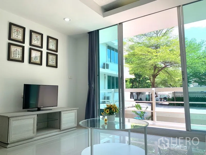 Condominium for rent or sale in Khlong Toei, Bangkok - Living room with TV stand and large sliding glass doors opening to a balcony with leafy views.