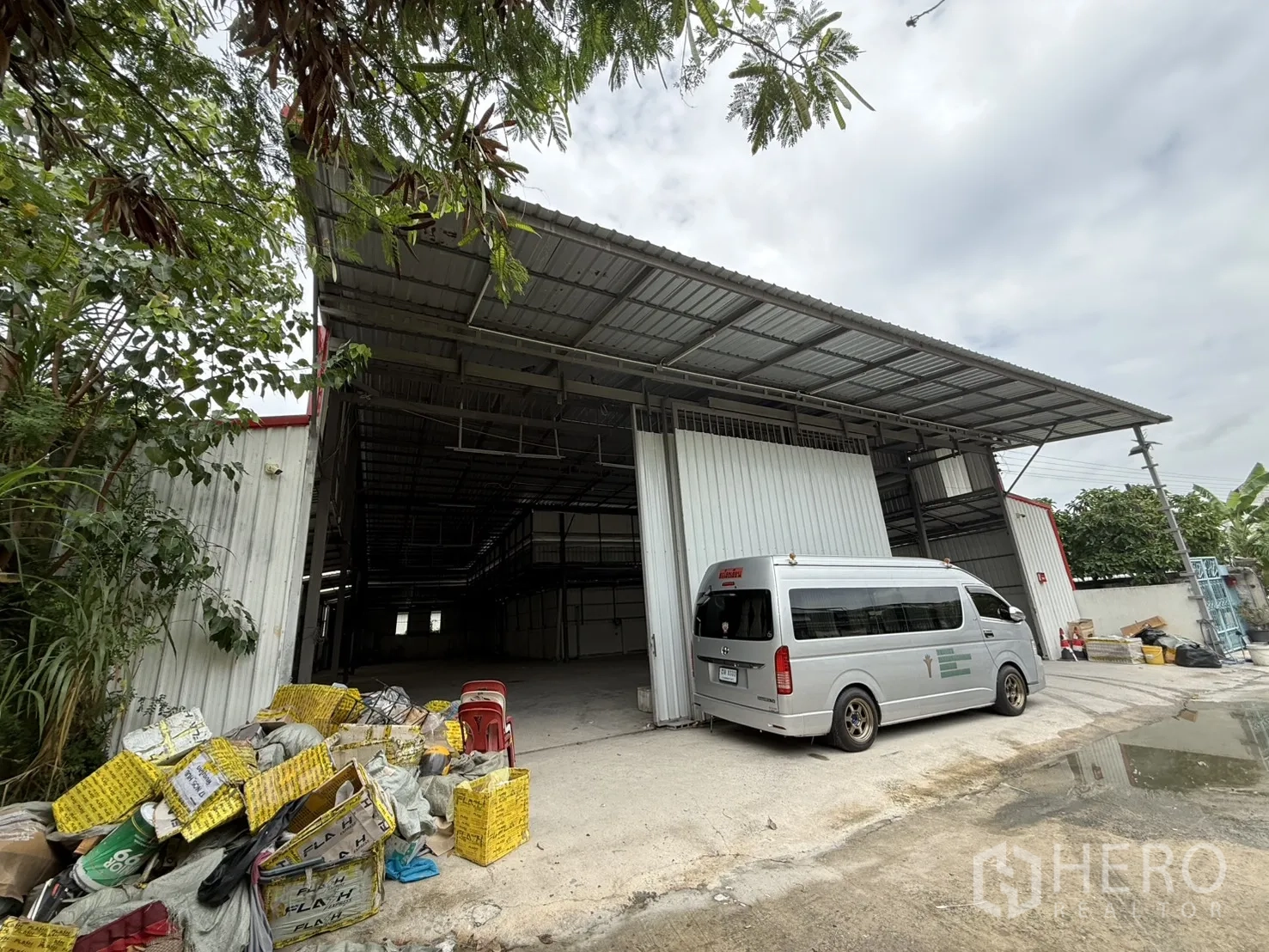 仓库 for rent in Huai Khwang, Bangkok - 仓库外观，钢结构建造，带宽敞遮雨装卸区与开启的推拉门，前方为混凝土场地与停靠车辆。