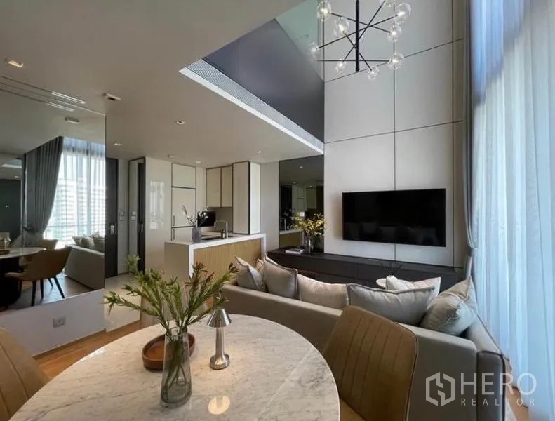 Condominium for rent in Khlong Toei, Bangkok - View from the dining table toward the kitchen and TV console with statement lighting and sheer curtains.