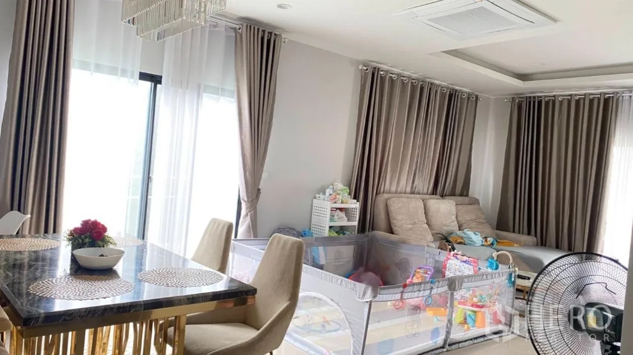 Detached House for rent or sale in Lam Luk Ka, Pathum Thani - Bright dining and lounge area with marble table, chandelier, large curtains, and a family playpen.