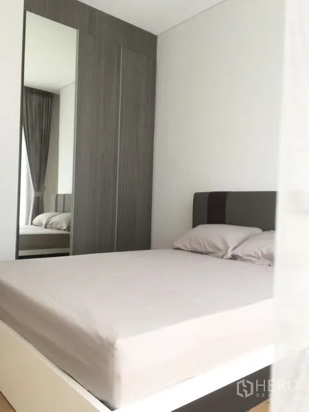 Condominium for rent or sale in Chatuchak, Bangkok - Cozy bedroom with a white bed, tall mirrored wardrobe and neutral décor.