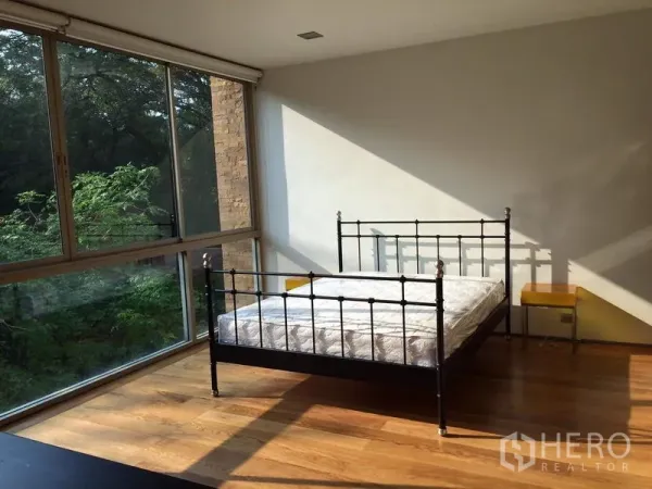 公寓 出租在Khlong Toei, Bangkok - 阳光充足的卧室，金属床架、木地板，转角落地窗望向绿景。