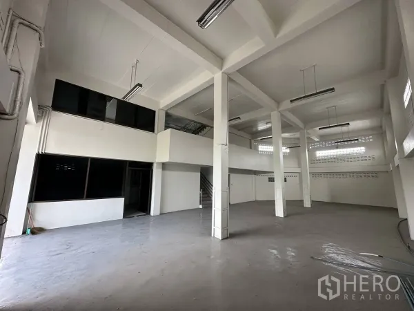 Home Office for rent in Taling Chan, Bangkok - High-ceiling ground floor warehouse space with strong columns, mezzanine windows and strip lighting.