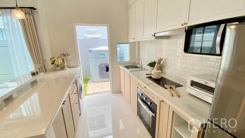 Townhouse for rent in Prawet, Bangkok - Galley kitchen with white cabinets, subway tile backsplash, built-in oven and a door to the rear yard.