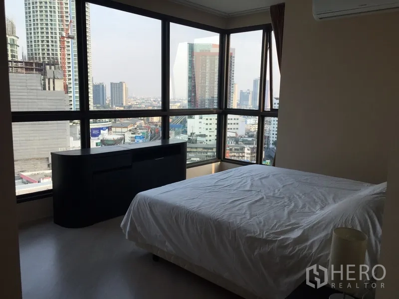 Condominium for rent in Khlong Toei, Bangkok - Corner bedroom with panoramic windows, double bed and air‑conditioning overlooking the Bangkok skyline.
