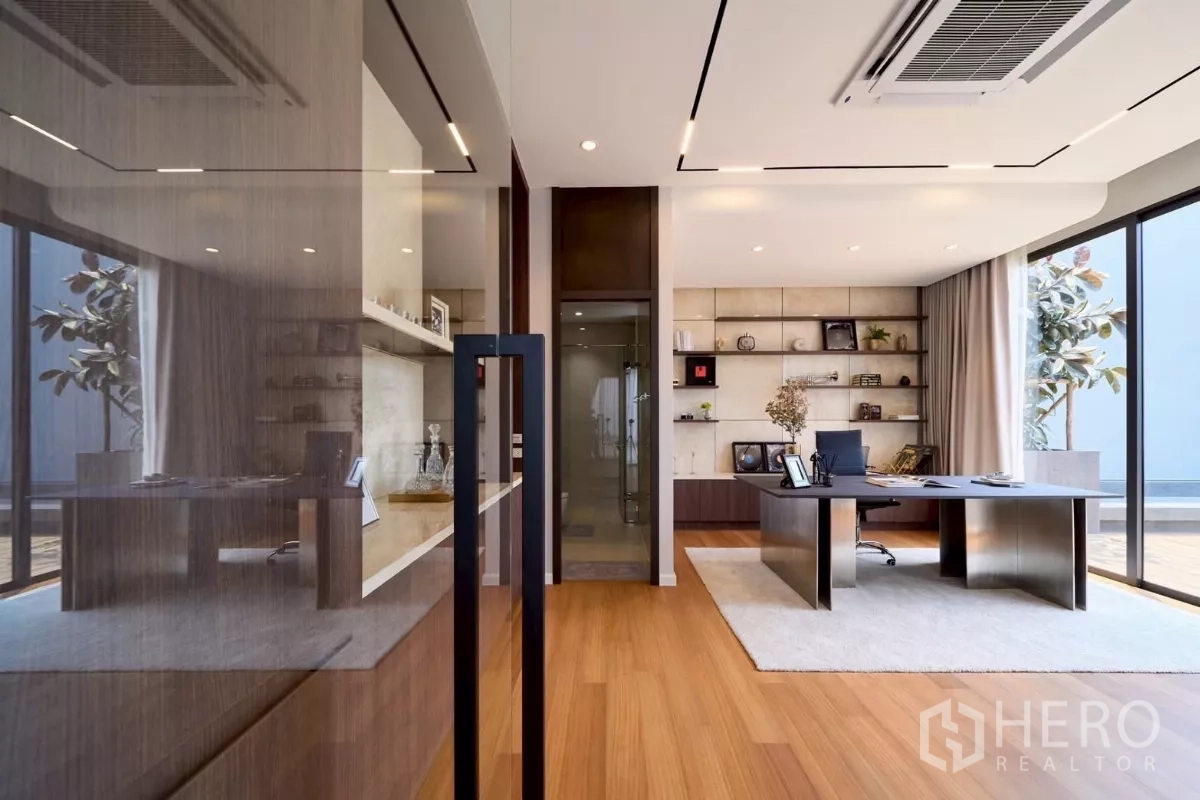 Detached House for sale in Lat Phrao, Bangkok - Home office with built-in shelving, oversized desk and floor-to-ceiling glazing.