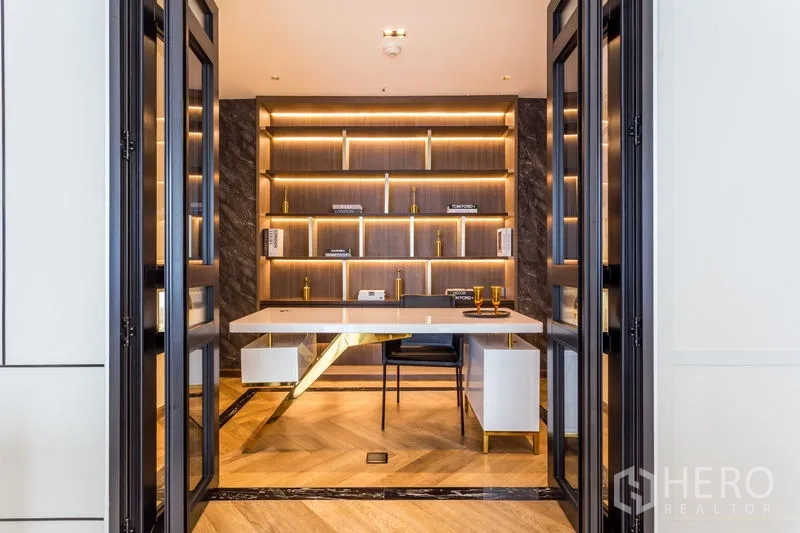 Condominium for rent in Khlong Toei, Bangkok - Modern home office with glass doors, backlit wood shelving and a marble-accent desk.