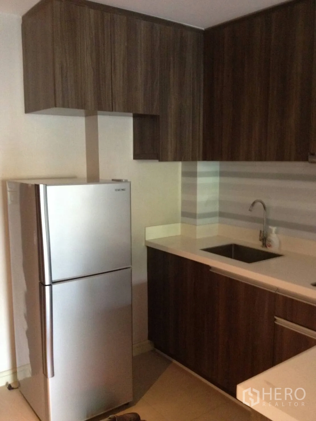 Condominium for rent in Khlong Toei, Bangkok - Kitchen with stainless refrigerator, sink and ample upper cabinets for storage.