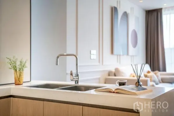 Condominium for rent in Khlong Toei, Bangkok - Modern open kitchen island with double sink and chrome faucet facing the airy living area.